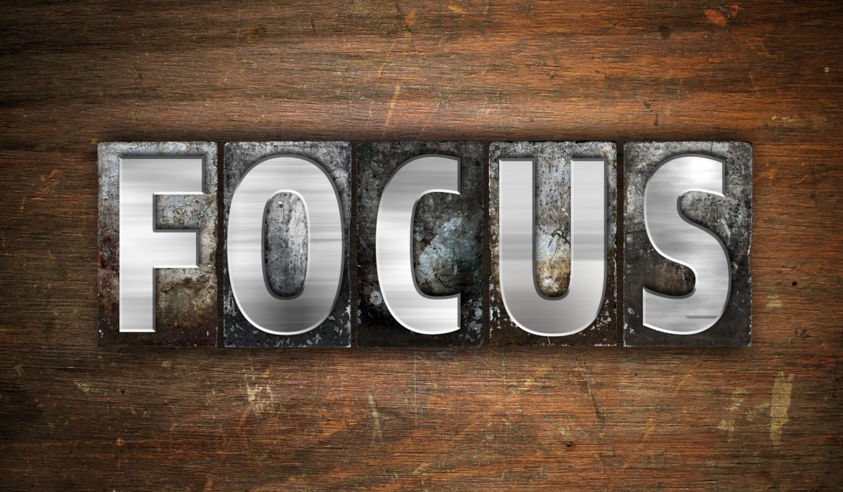 The word "Focus" written in vintage metal letterpress type on an aged wooden background.