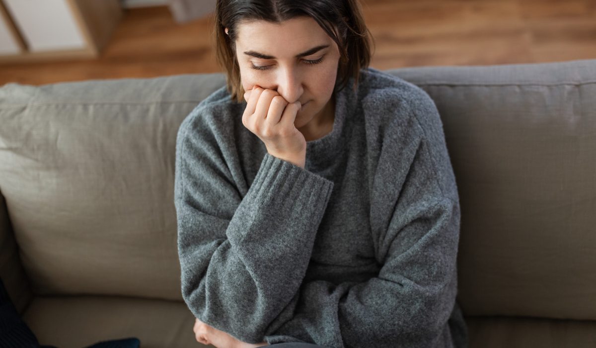mental health, psychological problem and depression concept - stressed woman sitting on sofa at home