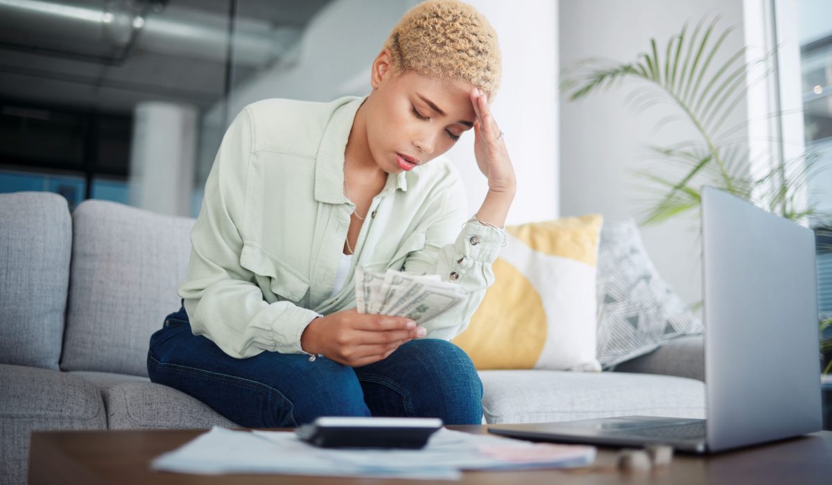 Woman, headache and stress for money, home budget or income on sofa with inflation, rent or bills. African person with depression, sad or confused for laptop cash debt, loan payment or cost of living.