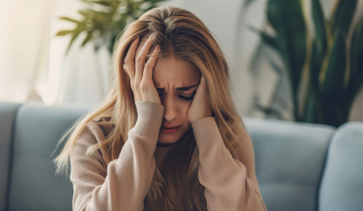 A woman sitting on a couch, visibly distressed, holding her head in her hands.