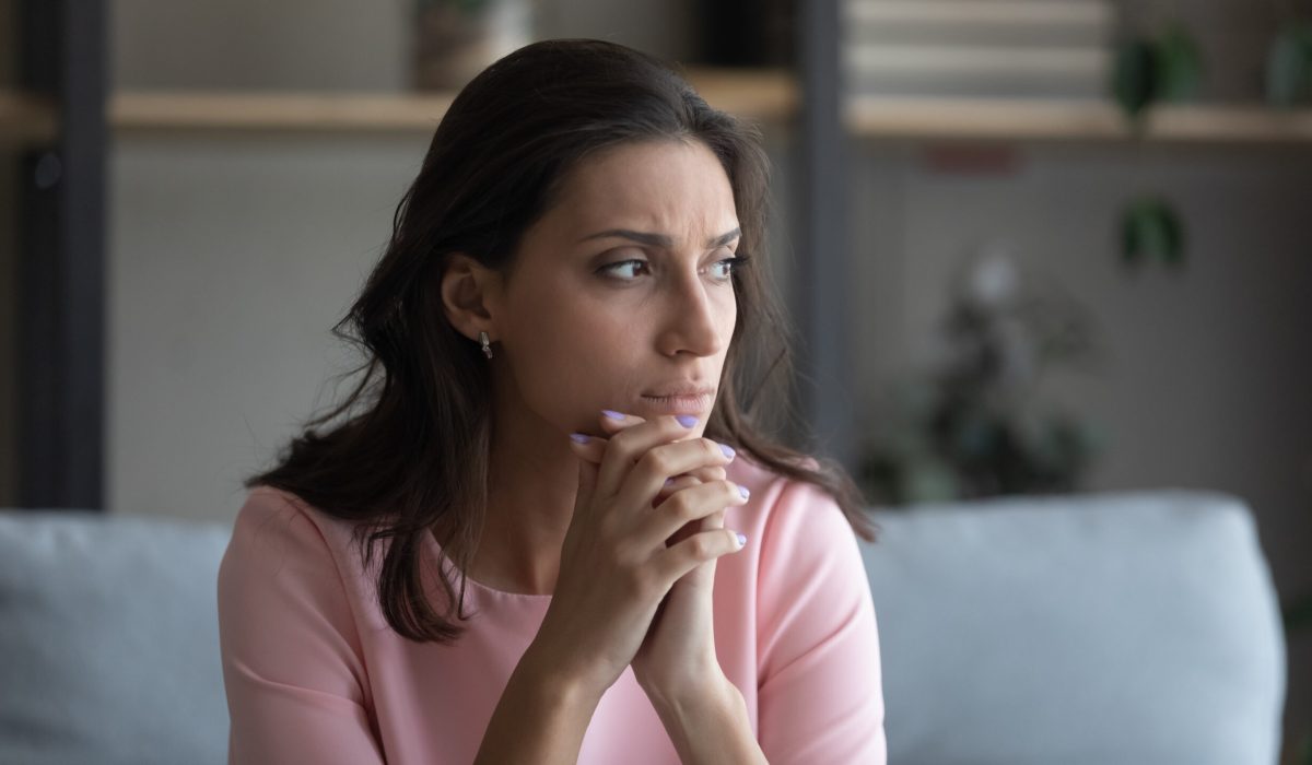 Worried young indian Arabic woman sit on couch at home look in distance thinking pondering, anxious unhappy arab mixed race female suffer from mental psychological personal problems, mourn or yearn